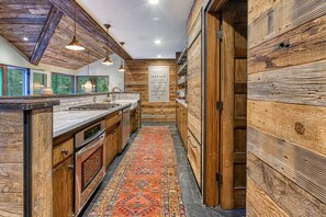 A kitchen with wooden walls, a tiled backsplash, and a patterned rug.