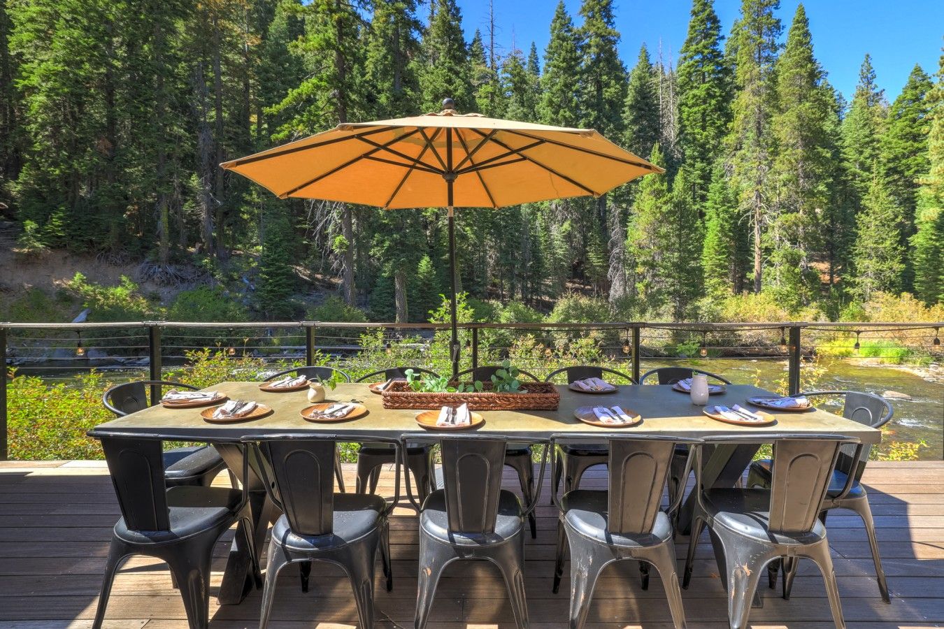 A dining table set outdoors with chairs, an umbrella, and a view of a forested area.