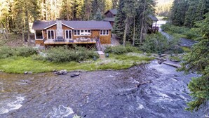 A lodge with a deck and a stone fireplace, surrounded by forest.