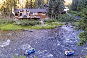 A lodge with a deck and a stone fireplace, surrounded by forest.