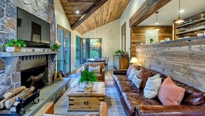 A cozy living room with a stone fireplace, leather sofa, wooden coffee table, and a dining area with a wooden table and chairs.