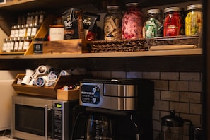 A kitchen with a coffee maker, a microwave, and shelves stocked with coffee beans and spices.