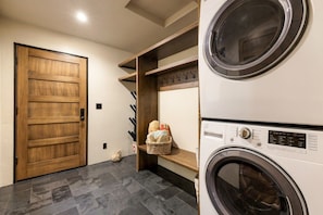 A laundry room with two stacked washing machines, a wooden door, and a shelf with hooks.