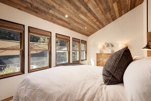 Ein Schlafzimmer mit einem großen Bett, Holzboden und mehreren Fenstern.