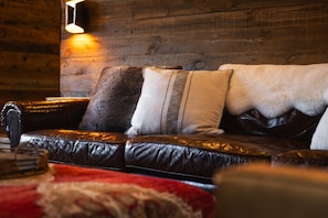 A leather sofa with multiple cushions against a wooden wall, a hanging light fixture, and a red patterned rug.