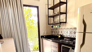 A compact kitchen with a refrigerator, stove, and a shelf unit. - Pousada Astral (Imbituba)