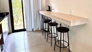 A modern kitchen with a white countertop, black stools, and a hanging light bulb. - Pousada Astral (Imbituba)