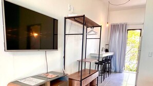 A modern living room with a flat-screen TV, a wooden entertainment unit, a dining area with chairs, and a large window with curtains. - Pousada Astral (Imbituba)