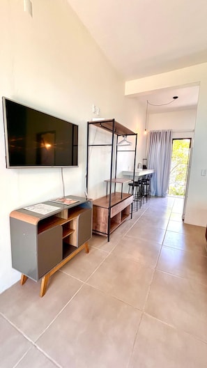 Een moderne woonkamer met een flatscreen televisie, een houten tv-meubel, een eethoek met stoelen en een groot raam met gordijnen.