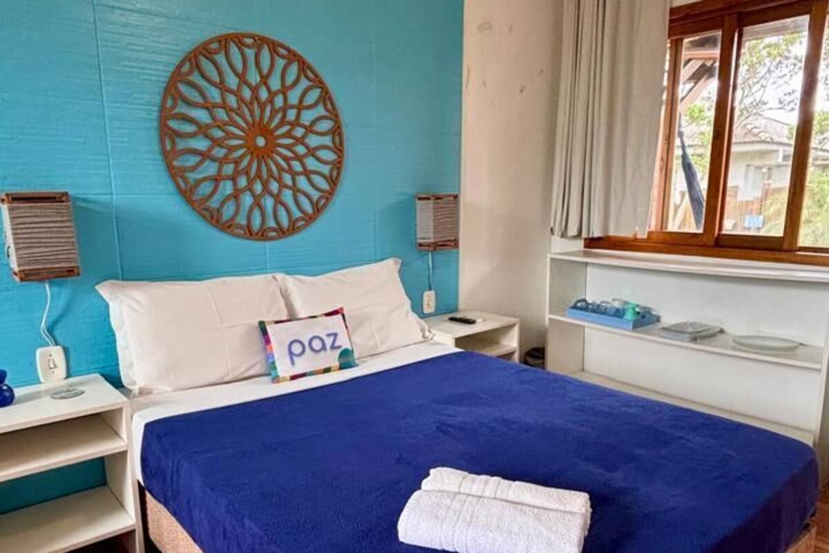 A bedroom with a bed, a decorative wall piece, a window with curtains, a bedside table, and a nightstand.