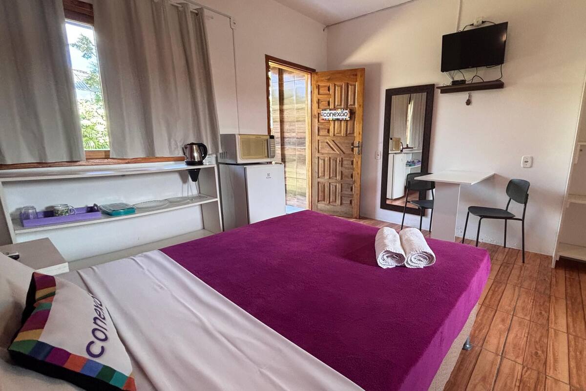 A hotel room with a bed, a desk, a chair, a television, and a wooden door.