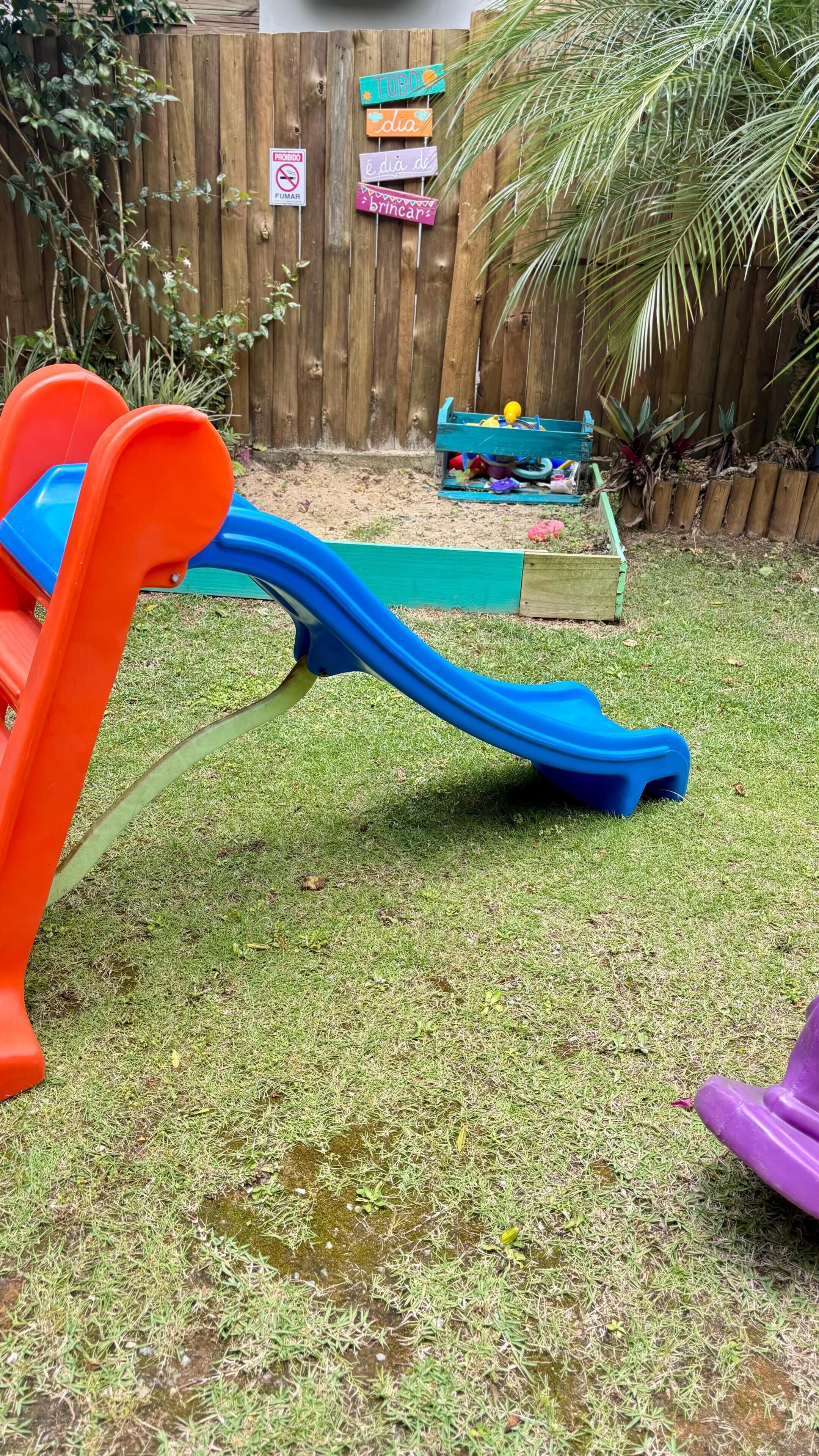 A backyard with a slide, a wooden fence, and a small play area with toys.