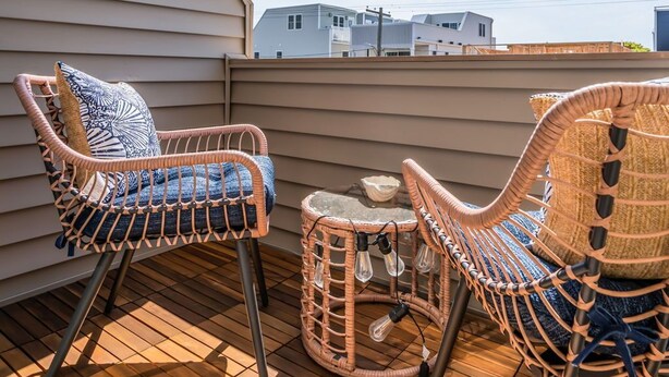 Un terrazzo in legno con sedie in vimini e un piccolo tavolo, con vista su una zona residenziale.