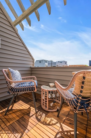 Une terrasse en bois, avec des chaises en osier et une petite table, donnant sur un quartier résidentiel.