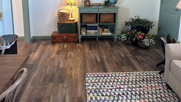 A living room with a flat-screen TV, wooden flooring, a patterned rug, and various wall decorations.