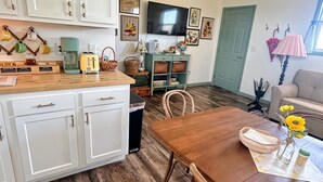 A kitchen with white cabinets, a wooden dining table, wicker chairs, a TV, and a green door. - Cottontail Cottage-Peaceful 1-bedroom cottage with AC in charming Lander (Lander)