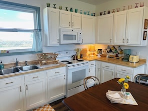 Una cocina con armarios blancos, microondas, estufa, lavaplatos y una mesa de comedor con un florero.