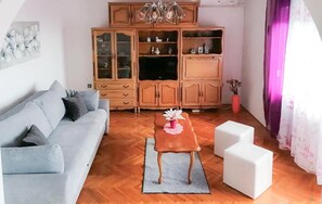 A living room with a grey sofa, a wooden cabinet, a small table with a flower, and white side tables. - Cozy apartment in Klenovica with house sea view (Klenovica)