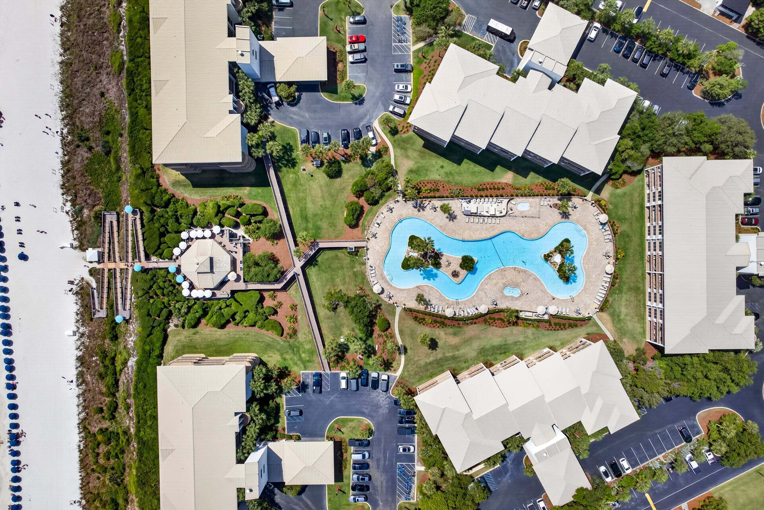 An aerial view of a resort with a swimming pool, parking areas, and buildings with flat roofs.
