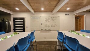 Une salle de conférence équipée d’un tableau blanc où sont énumérées les tâches à accomplir, de chaises bleues, d’une longue table et d’un plafond en bois.