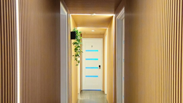 Un couloir aux murs recouverts de lambris en bois, une porte portant le numéro 2 et une plante accrochée au mur.