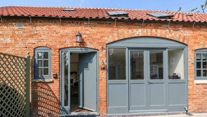 A brick building with a red-tiled roof, two grey double doors, and a small window with a lattice.