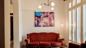Un canapé rouge dans une pièce dotée d’une grande fenêtre, d’un lustre et d’un tableau accroché au mur.