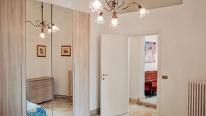 Une chambre avec un grand miroir, une commode en bois, un lit avec une literie à motifs, une chaise rouge et un radiateur.