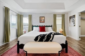 Una camera d'albergo con un letto, una panca, una finestra con tende, un muro decorato e una porta.