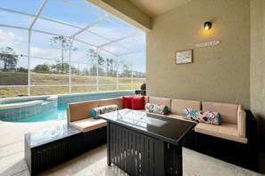 Ein Poolbereich mit einer verglasten Terrasse, einer Couch mit bunten Kissen und einem Tisch.