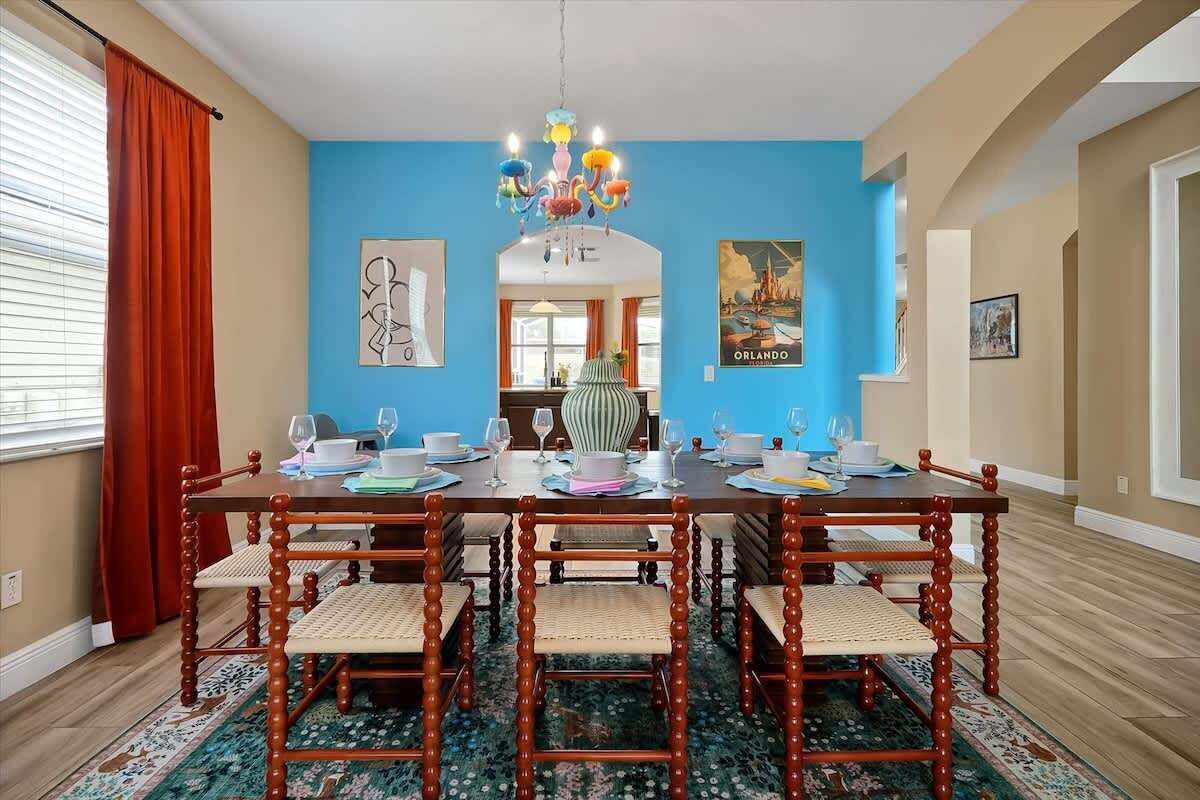 A dining room with a wooden table set for six, surrounded by chairs, a chandelier, and artwork on the walls.