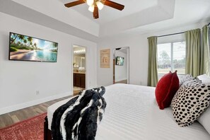 Ein Schlafzimmer mit einem großen Bett, einem Deckenventilator, einem Fernseher und einem Fenster mit Vorhängen.