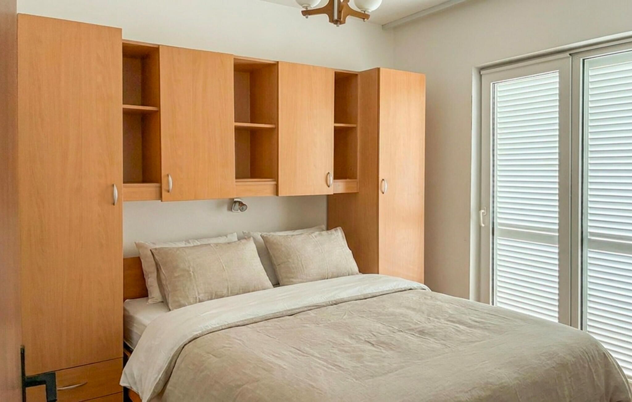 A bedroom with a bed, a wardrobe, and a window with blinds.