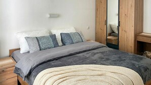Quarto com cama, almofadas, mesa de cabeceira e guarda-roupa.
