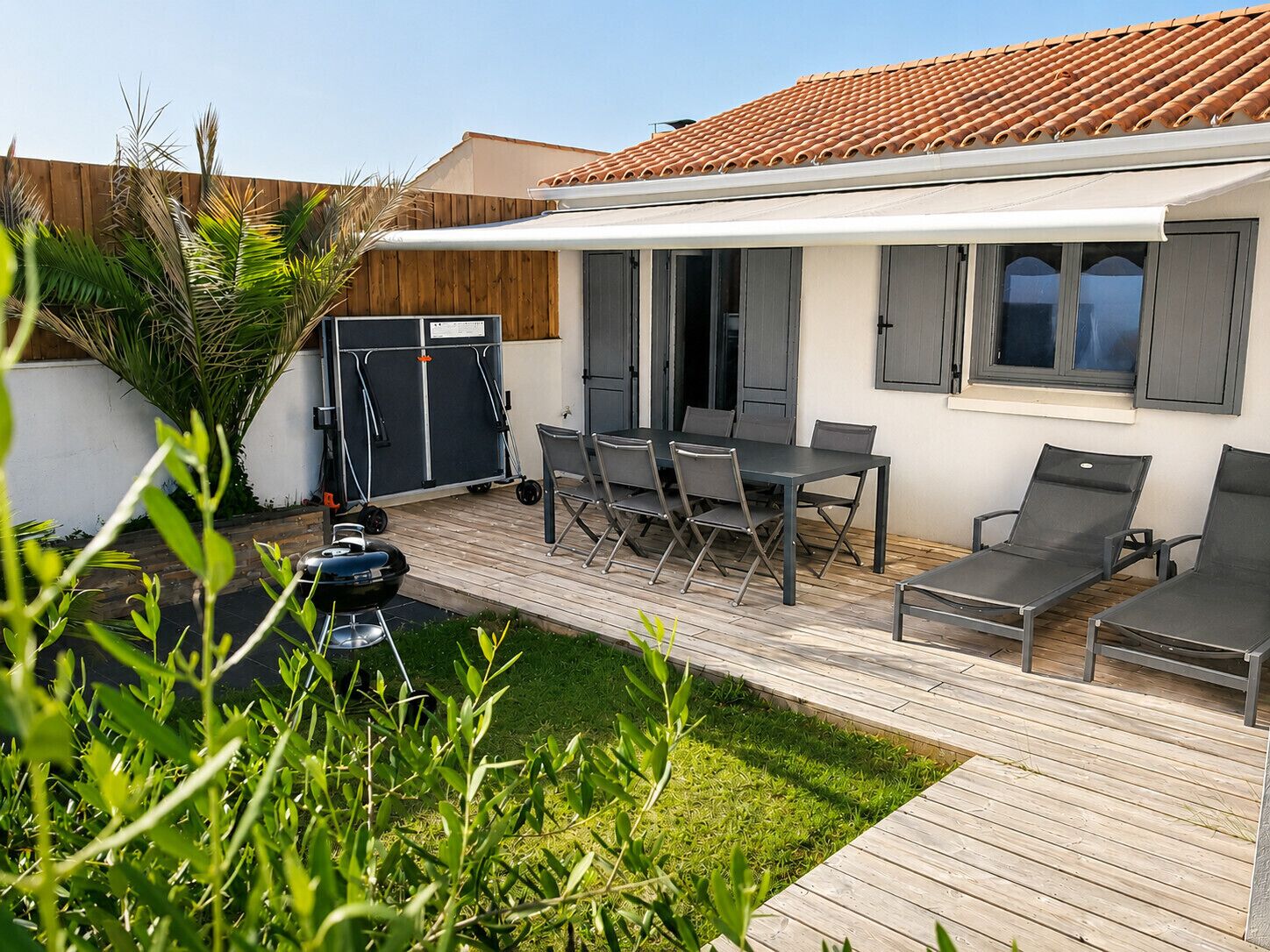 A patio with a table and chairs, a grill, and a wooden deck.