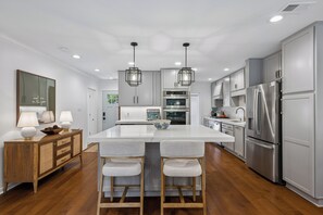 Eine moderne Küche mit einer zentralen Kochinsel, Barhocker, einem Holzsideboard und Edelstahlgeräten.