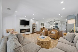 Ein modernes Wohnzimmer mit Kamin, Sofas, einem Couchtisch und einer Küche im Hintergrund.