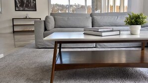 Ett modernt vardagsrum med en grå soffa, ett soffbord i trä och en krukväxt.