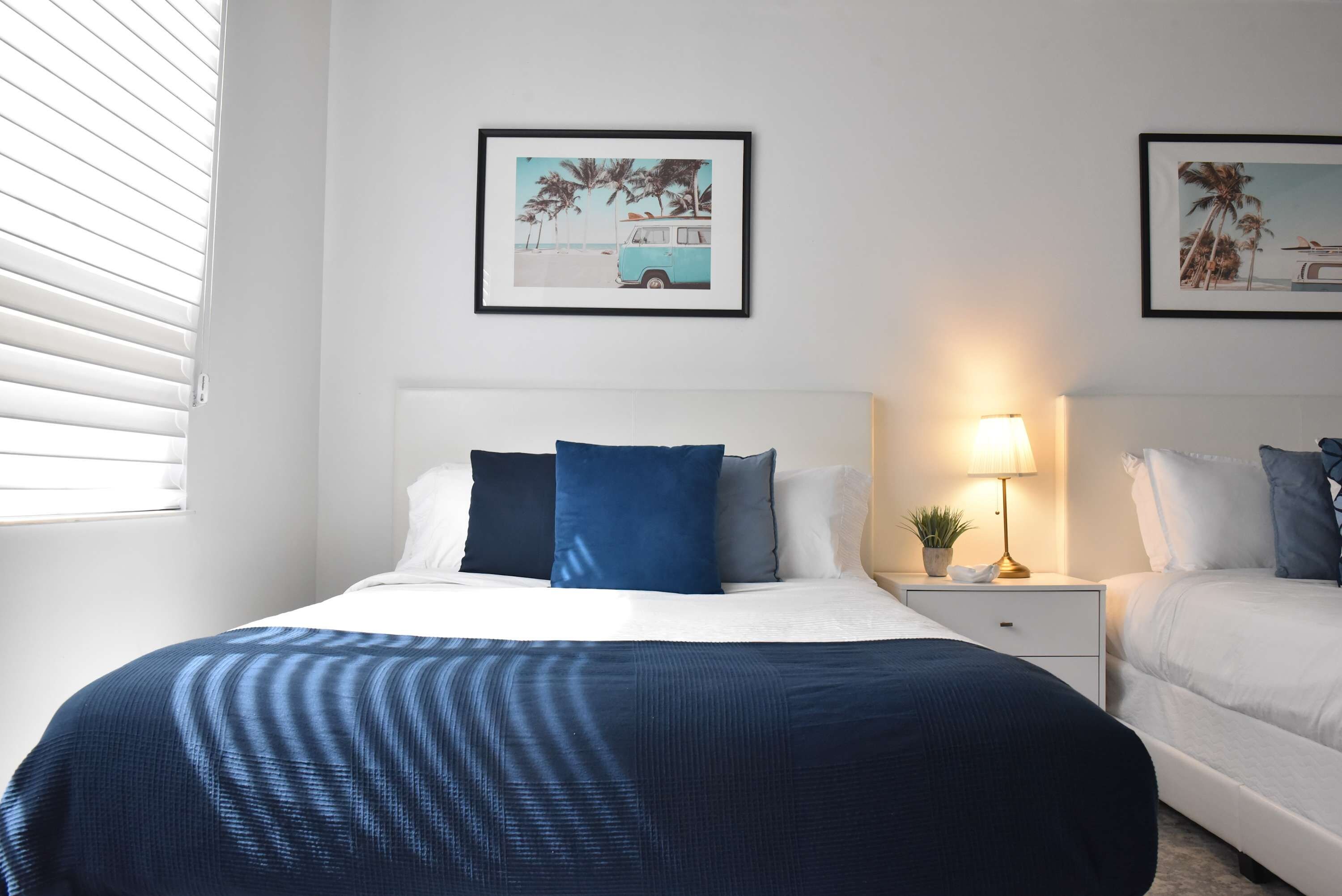 A hotel room with a bed, a bedside table with a lamp, and two framed pictures on the wall.
