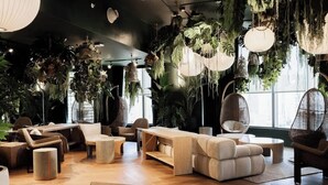 Un área de estar moderna con asientos, plantas colgantes y ventanas amplias.