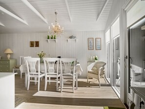 Ein Essbereich mit einer Chandelüster, weißen Stühlen, einem Tisch und einem Korbstuhl.