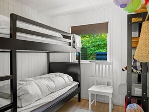 Ein Schlafraum mit Etagenbetten, einem Fenster, einem weißen Stuhl und einem Regal mit Gegenständen.
