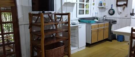 A kitchen with white cabinets, a wooden chair, a television, and a window.