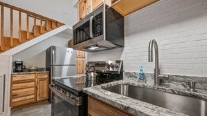 A modern kitchen with stainless steel appliances, a granite countertop, and a wooden staircase. - Walk to Attitash in 2 Mins | Cozy Mountain Condo (Bartlett)
