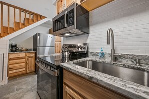 A modern kitchen with stainless steel appliances, a granite countertop, and a wooden staircase. - Walk to Attitash in 2 Mins | Cozy Mountain Condo (Bartlett)