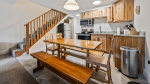 A modern kitchen with wooden cabinets, a dining table, and a bench. - Walk to Attitash in 2 Mins | Cozy Mountain Condo (Bartlett)