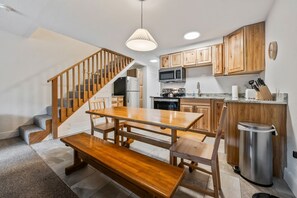 A modern kitchen with wooden cabinets, a dining table, and a bench. - Walk to Attitash in 2 Mins | Cozy Mountain Condo (Bartlett)