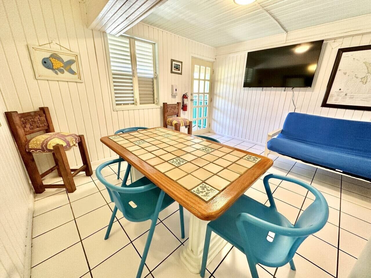 A room with a tiled floor, a wooden table with chairs, a blue sofa, a television, and a framed picture on the wall.