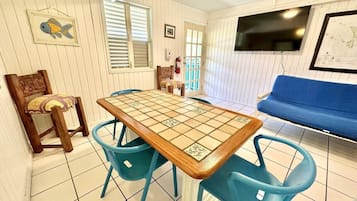A room with a tiled floor, a wooden table with chairs, a blue sofa, a television, and a framed picture on the wall.
