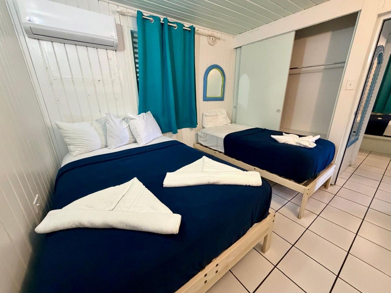 A room with two beds, a mirror, a wardrobe, and an air conditioning unit.